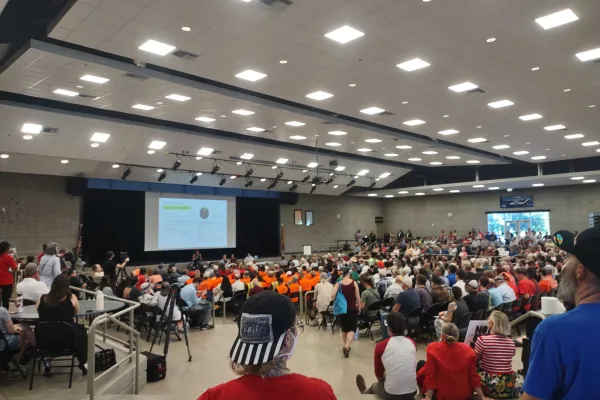 Scene from a city-wide Tucson meeting on Project Blue. Hundreds of participants pack chairs and sit on the floor facing a projector screen displaying data.