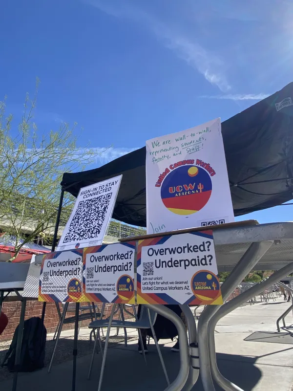 Several UCWAZ signs on a table outside. One says "Overworked? Underpaid? Join your union!" Another is a QR code. One is a sign with UCWAZ logo.