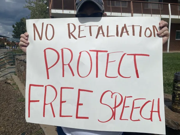 Picture features a person holding a sign that mostly obstructs their body. The sign reads "no retaliations, protect free speech."