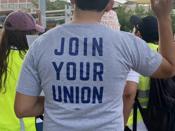 Picture of the back of someone's shirt. The person holds up a fist in solidarity. The shirt reads "join your union."