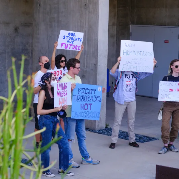 People standing outside of a concrete building, holding signs in protest.